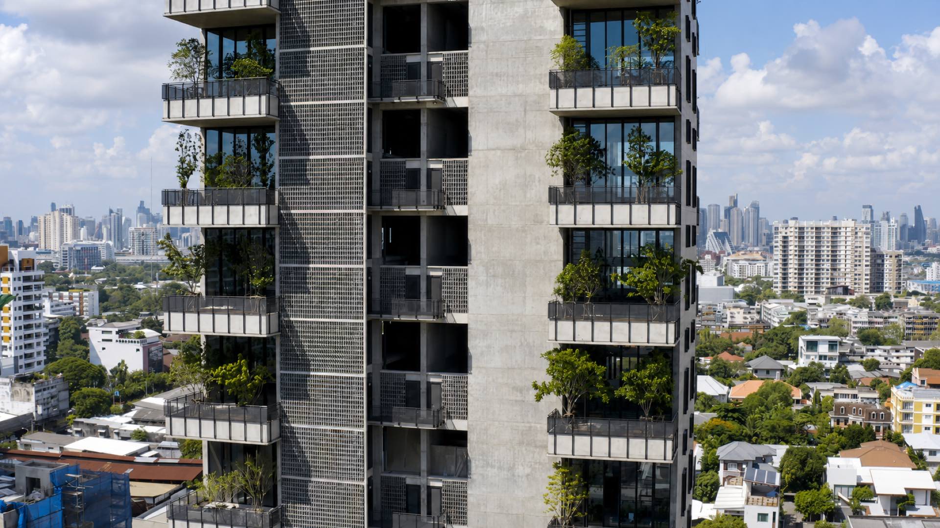 Windshell Naradhiwas: the tower's planted balconies and perforated concrete facade against the Bangkok skyline, seen from mid-height